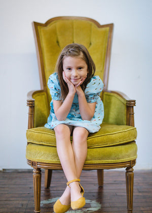 Girl wearing Puff sleeve dress in swimmers print sitting in chair looking at camera.  Puff sleeve dress is featured in Easter Gift guide by Worthy Threads, unique toddler clothing brand.