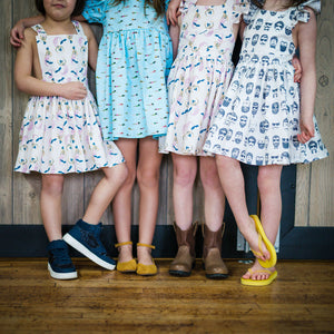 Four girls from the neck down wearing a variety of dresses and patterns.  Unique kids clothing!