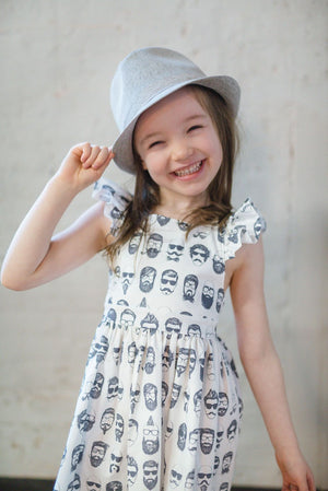 Girl wearing Beatnik ruffle sleeve dress and hat laughing.  Unique kids clothes available in coordinating sibling outfits!