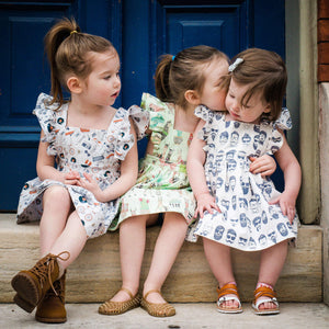 Unique Baby Clothes and matching sibling outfits.  Three toddlers wearing vintage style dresses sitting on a step in front of blue door.