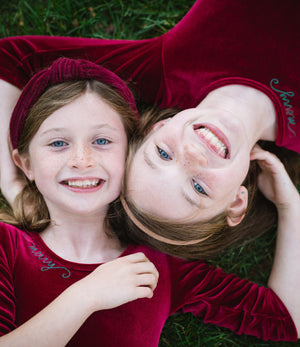 Sister in matching christmas twirly dresses in burgundy velvet with embroidery