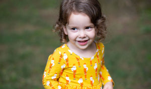 Toddler wearing Christmas outfit featuring Santa Claus on a mustard yellow background. 