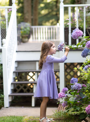 Girl modeling purple twirly dress while smelling purple flowers