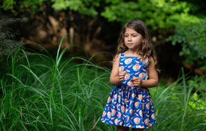 Toddler modeling girls pinafore dress in funky fun blue ramen print in grass