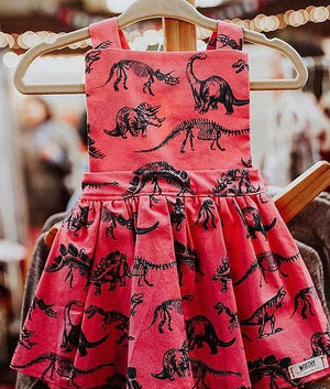 Close up shot of baby pinafore dress in dino print.  Girls dinosaur clothes available in matching sister outfits newborn and toddler!