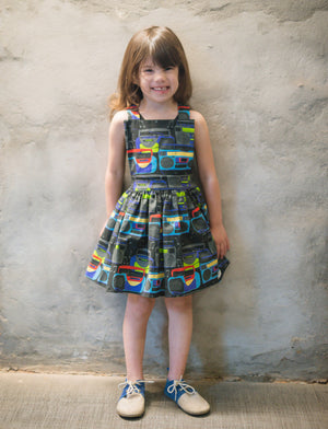 Girl modeling pinafore dress in boombox print: unique kids clothing by Worthy Threads brand