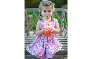 Model sipping lemonade in bright pink flamingo pinafore dress