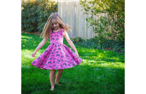 Girl modeling hot pink dinosaur print twirly dress with ruffle sleeves